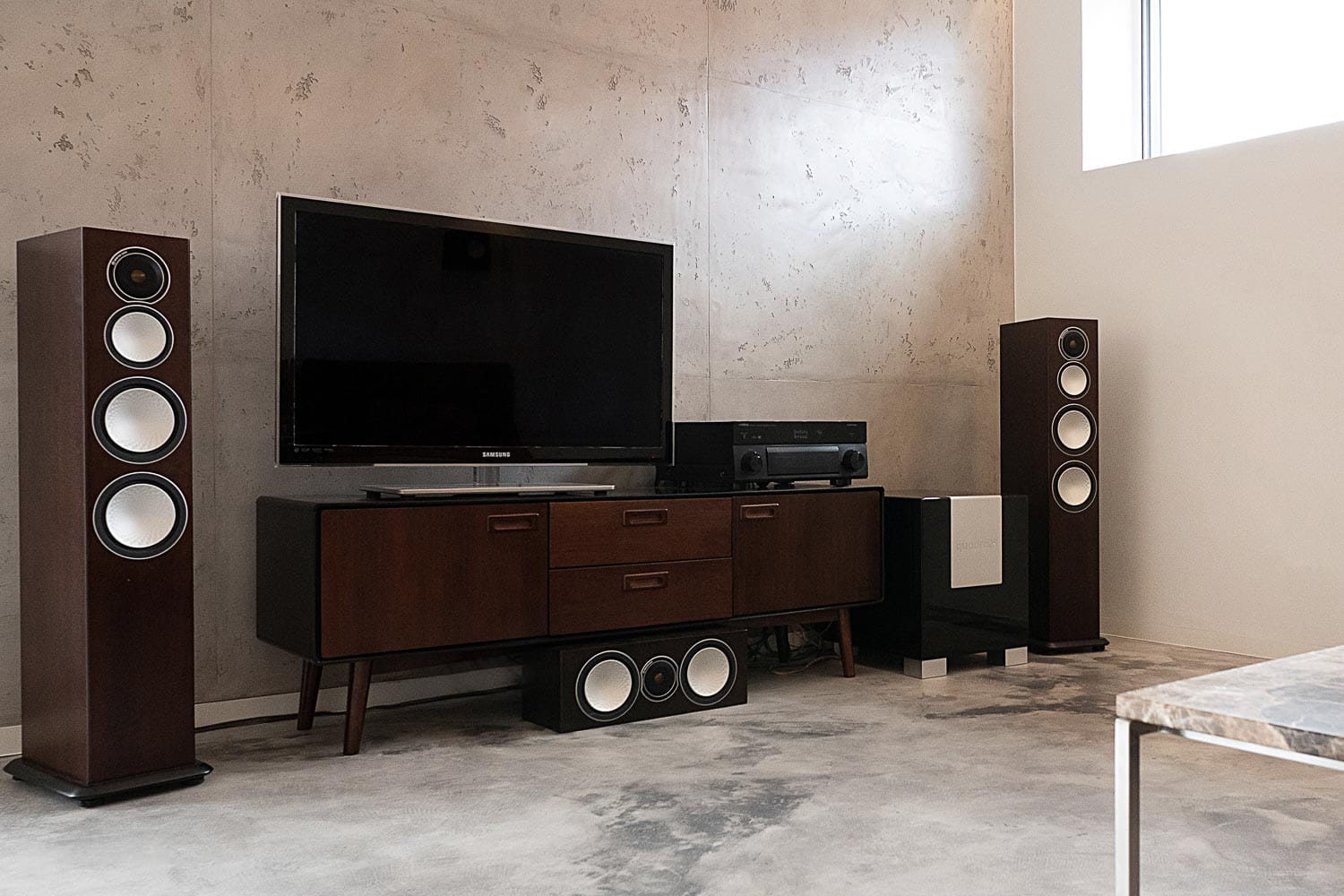 Wohnzimmerraum mit fugenlosem Boden und Wandputz in Betonoptik in dem eine Stereoanlage auf einem Sideboard steht.